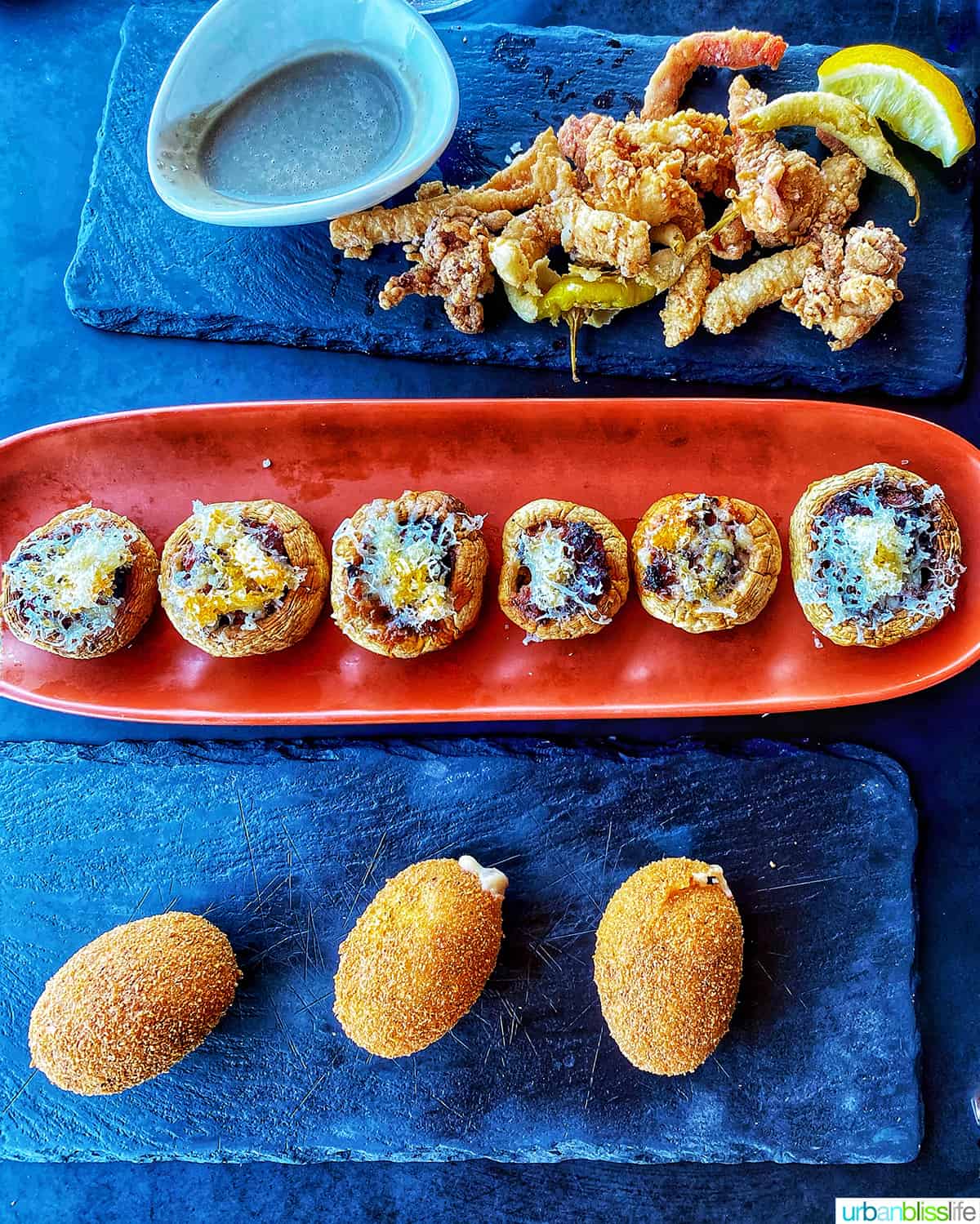 trio of Spanish tapas on black marble plates and one orange serving plate.