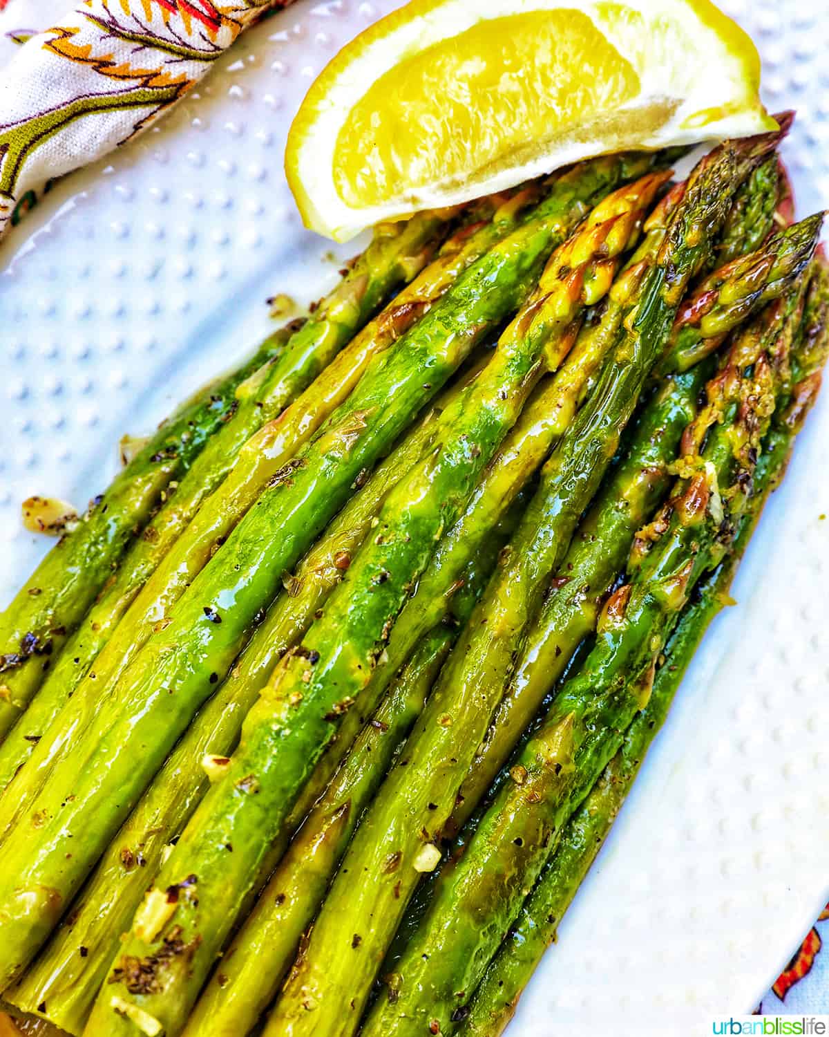 white serving plate with grilled asparagus, garlic, and lemon wedge.