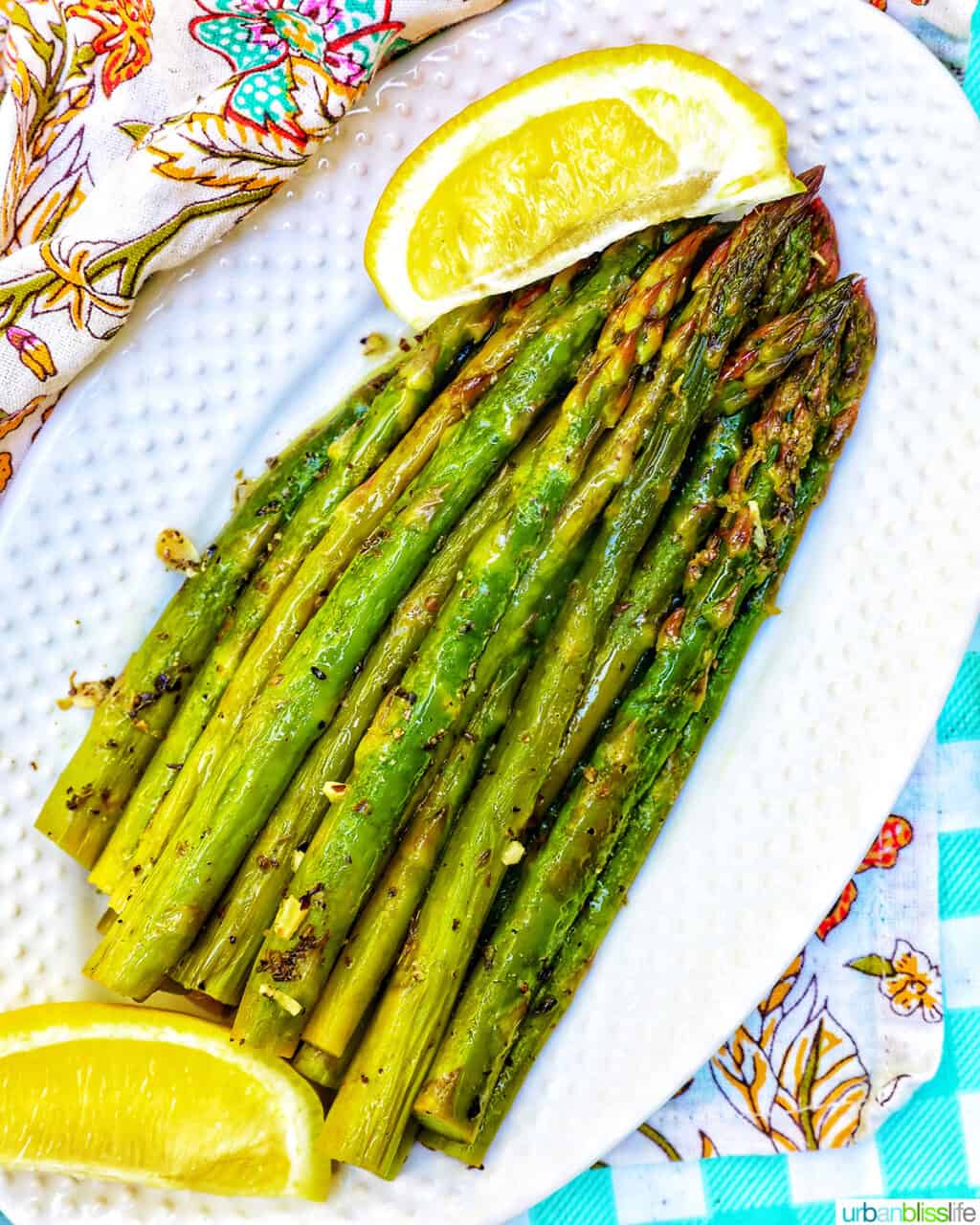 grilled asparagus with lemon wedges on a white plate and colorful napkin.