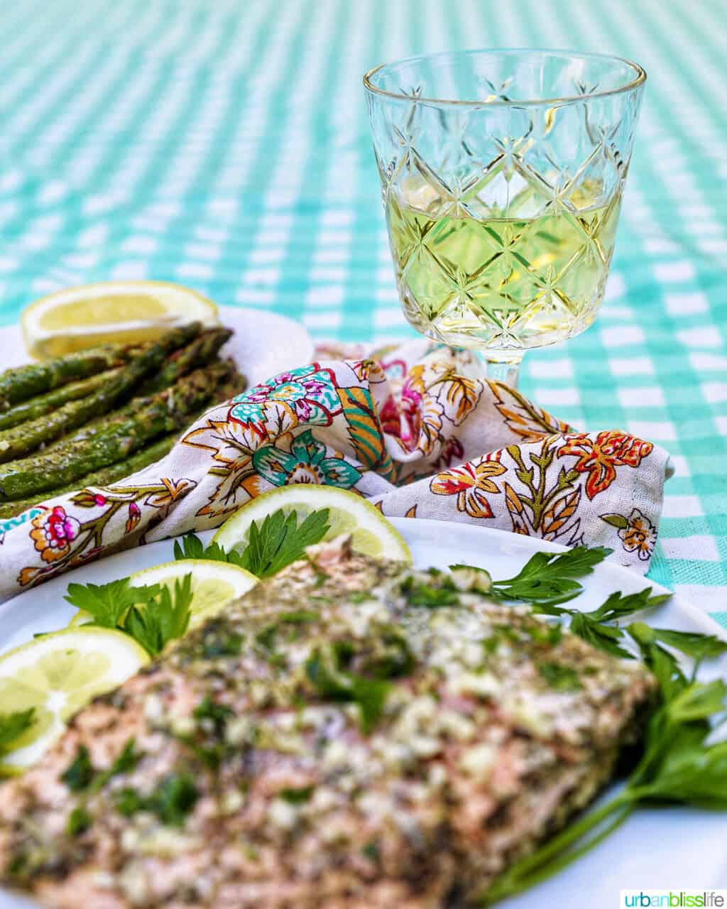 glass of white wine with salmon and asparagus on an aqua checkered tablecloth.