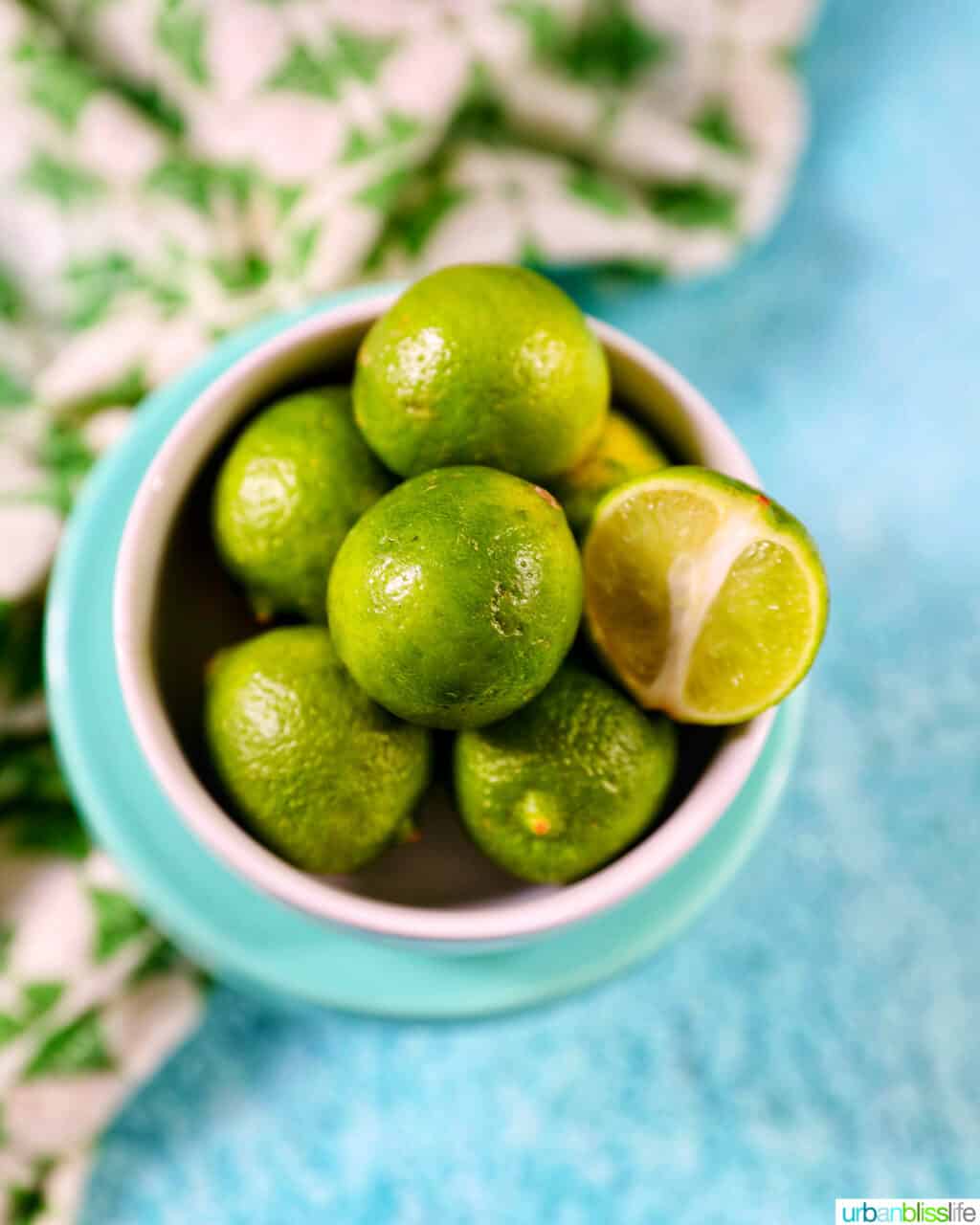 bowl of key limes on a blue background with green and white napkin.