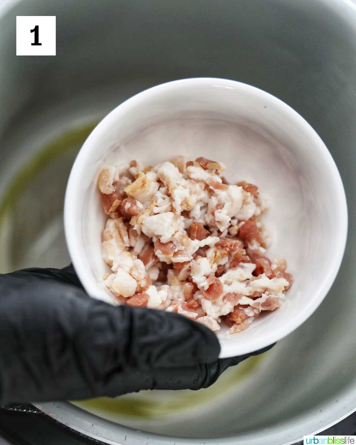 gloved hand holding a white bowl of chopped bacon over an Instant Pot
