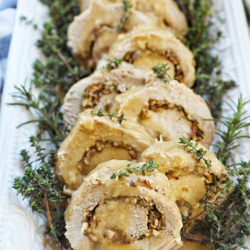 sliced stuffed pork loin on a white plate with a bed of herbs.