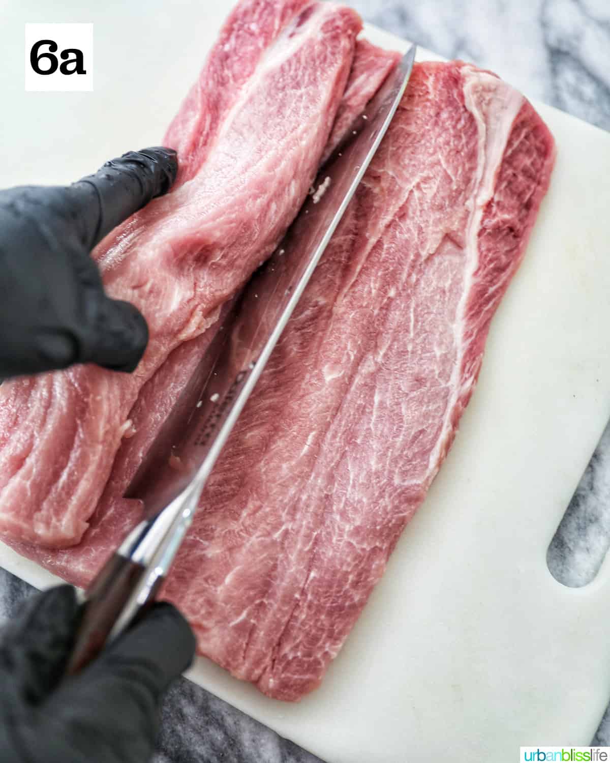 gloved hands slicing into the pork loin with a knife on a white cutting board.