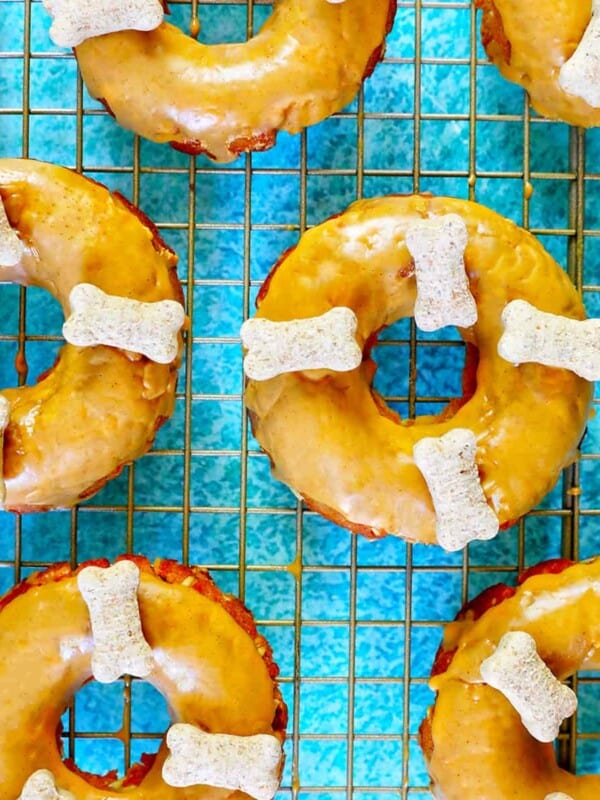 Glazed dog donuts with dog biscuits on a cooling rack on a bright blue table.