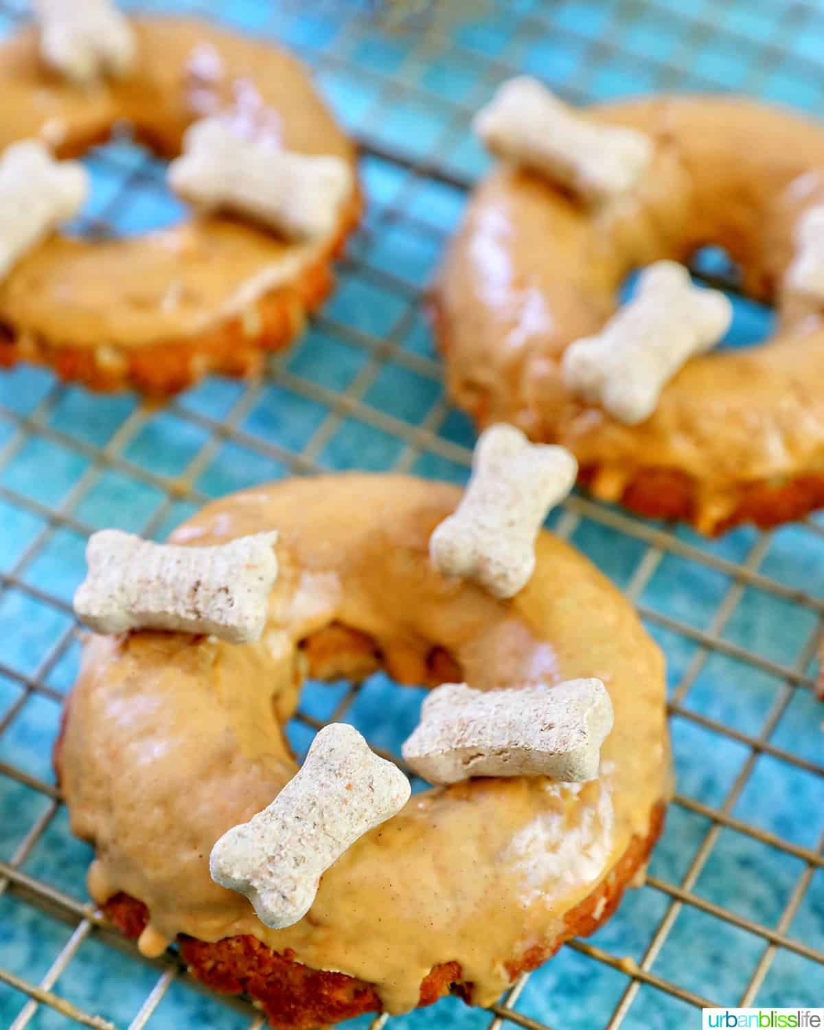 three glazed dog donuts with dog biscuits on a cooling rack.