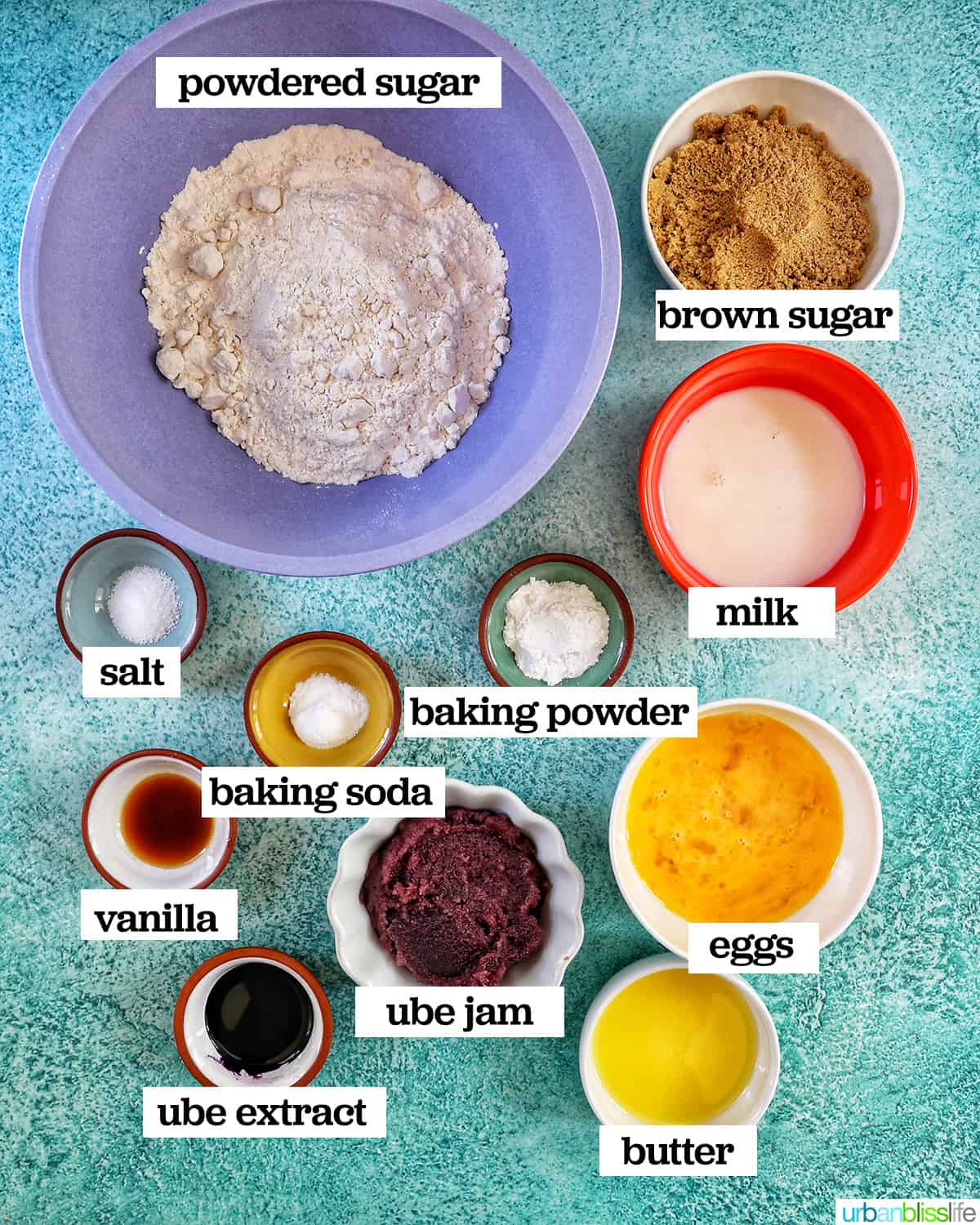several bowls of ingredients to make ube donuts on a blue table.