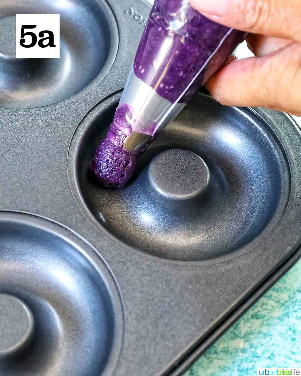 purple ube batter in a piping bag into a donut pan.