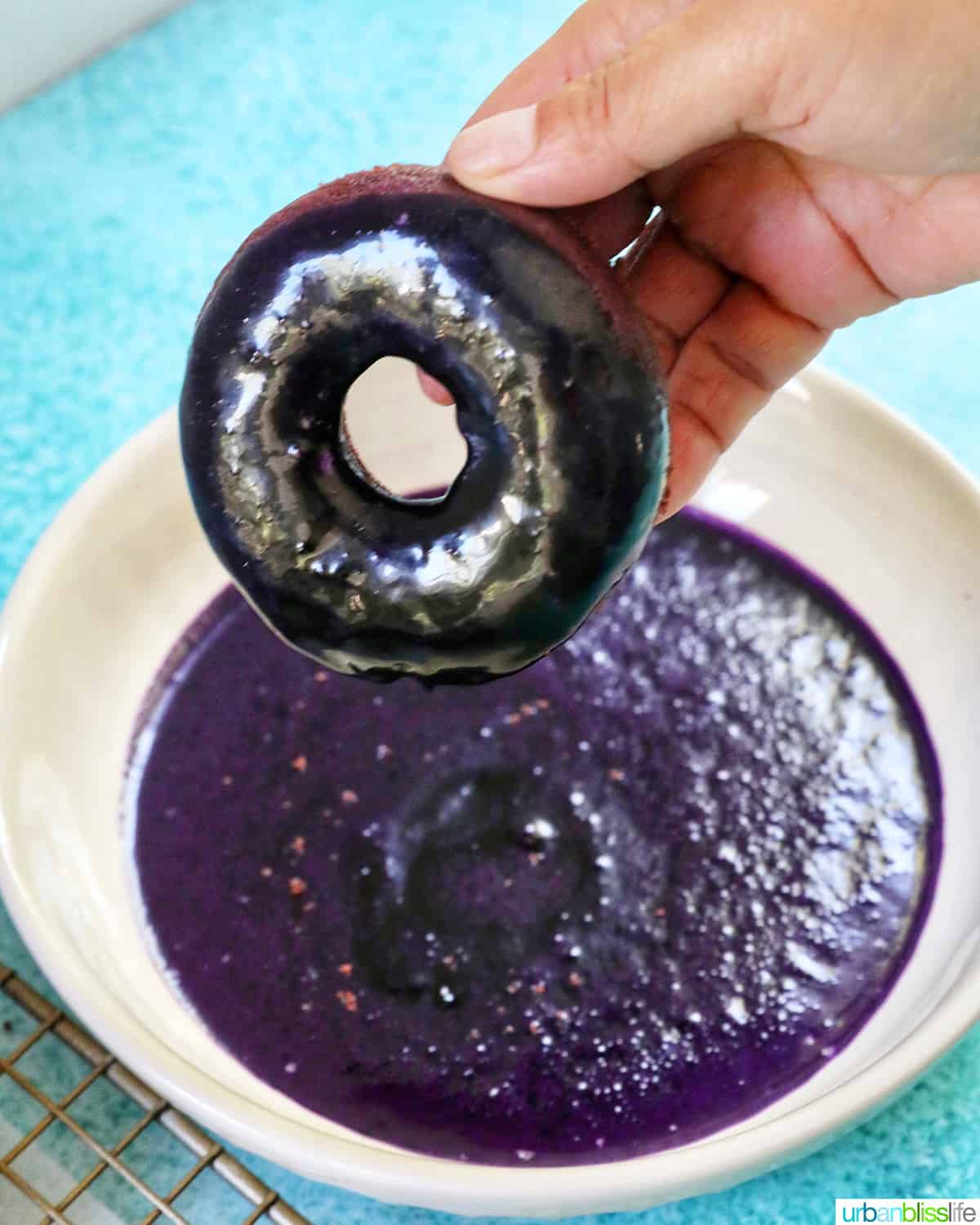 hand dipping purple ube donut into ube glaze.
