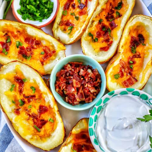 several air fryer potato skins with sides of green onions, bacon, and sour cream.