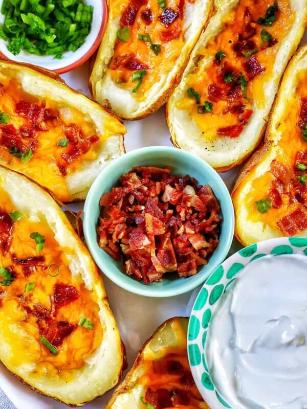 several air fryer potato skins with sides of green onions, bacon, and sour cream.