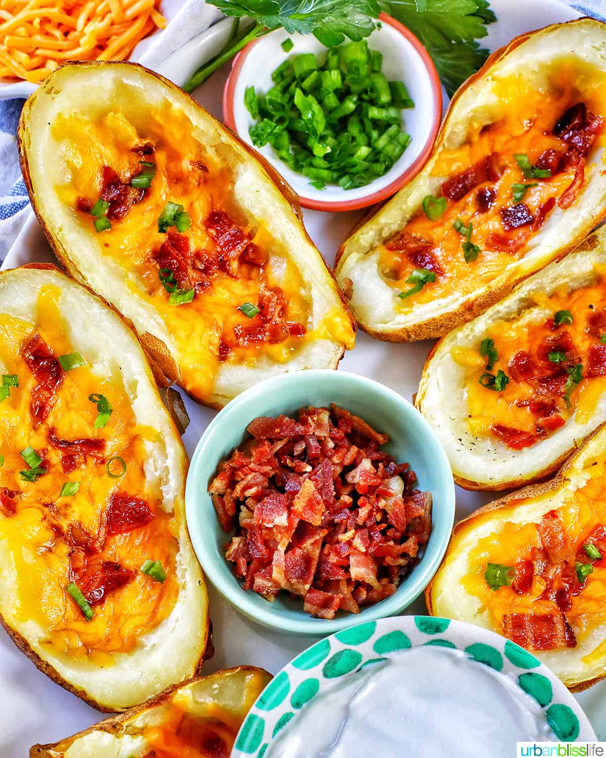 several air fryer potato skins with sides of green onions, bacon, and sour cream.