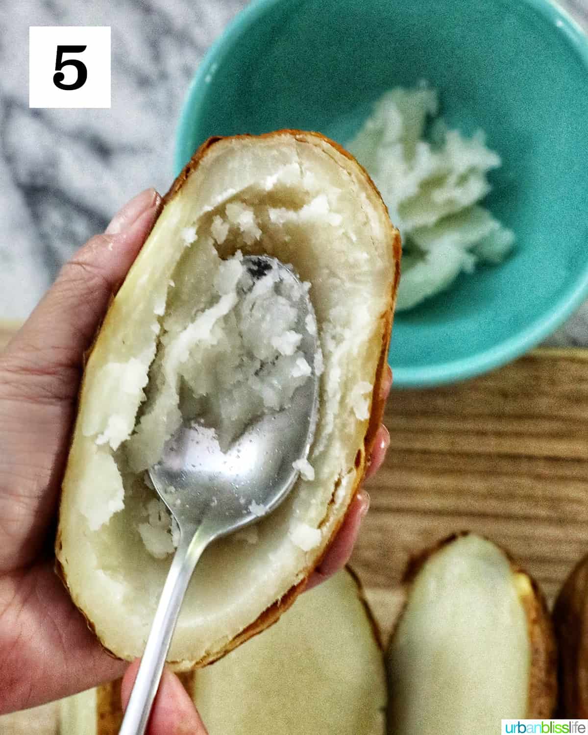 a spoon scooping out the center of a baked potato.