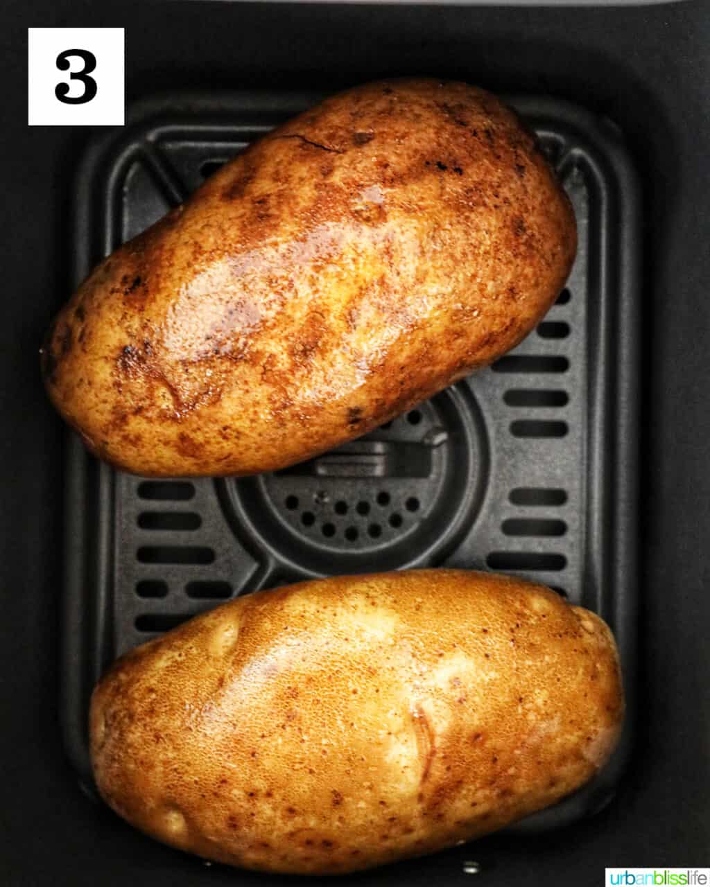 two potatoes in an air fryer basket.