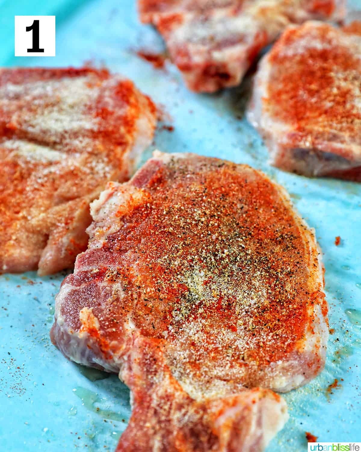 well seasoned pork chops on parchment paper on a bright blue table.