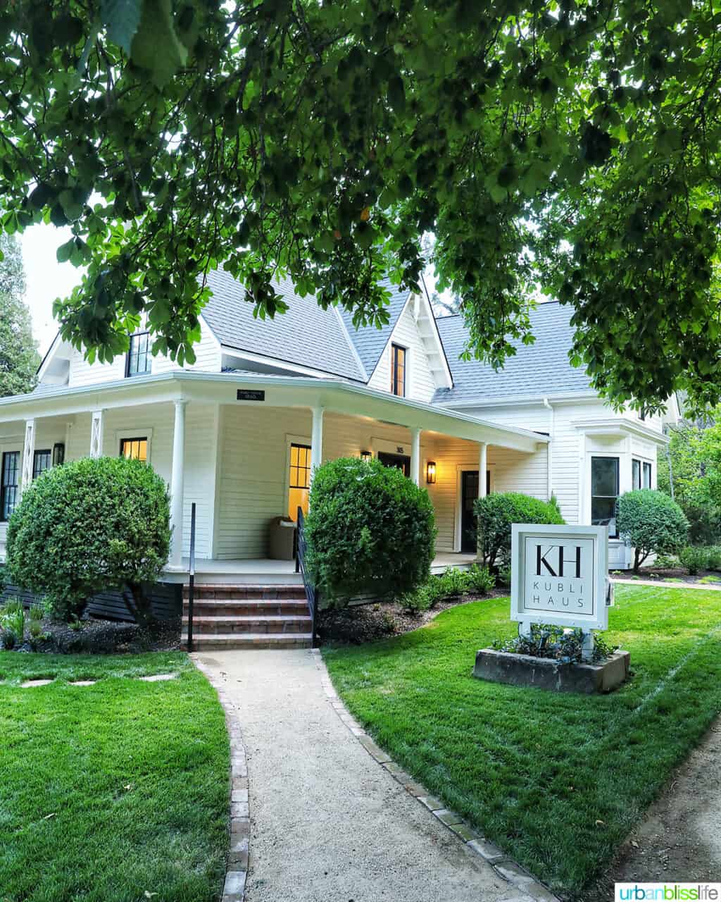 the exterior of Kublis Haus hotel in Jacksonville, Oregon with lush green lawn, walkway, and overhanging trees.