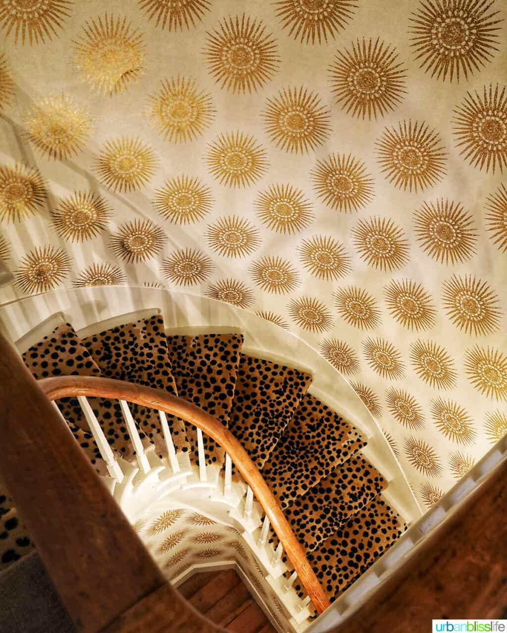 dramatic staircase with gold and cream wallpaper and animal print stair carpeting.