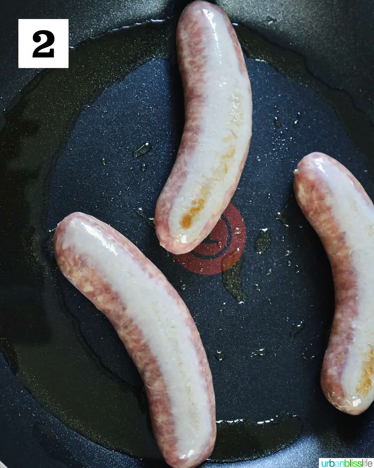 three sausage links cooking in a non-stick skillet.