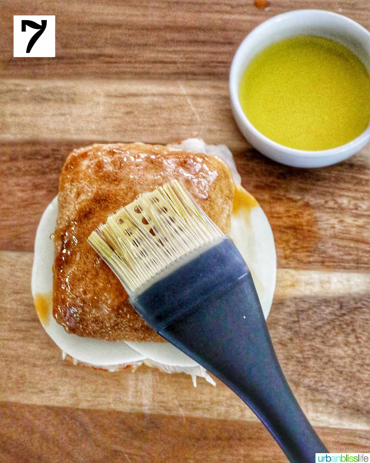 pastry brush brushing melted butter on the top of a turkey pesto sandwich.