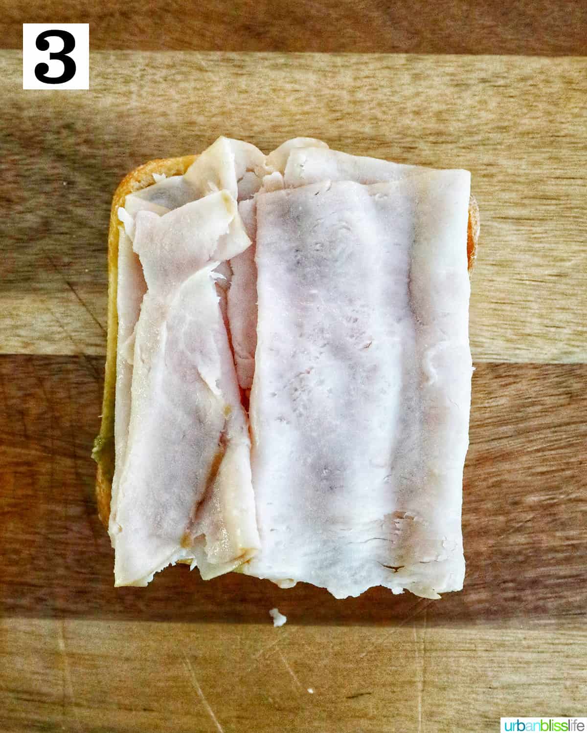 slices of turkey to make turkey pesto sandwich on a cutting board.