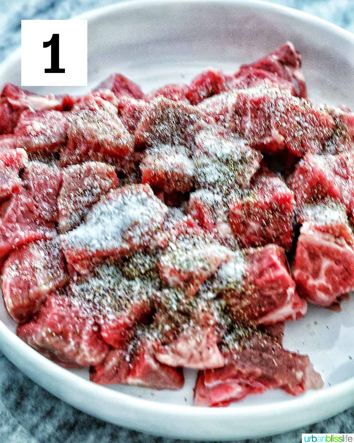 seasoned beef chunks with salt and pepper in a large white platter.