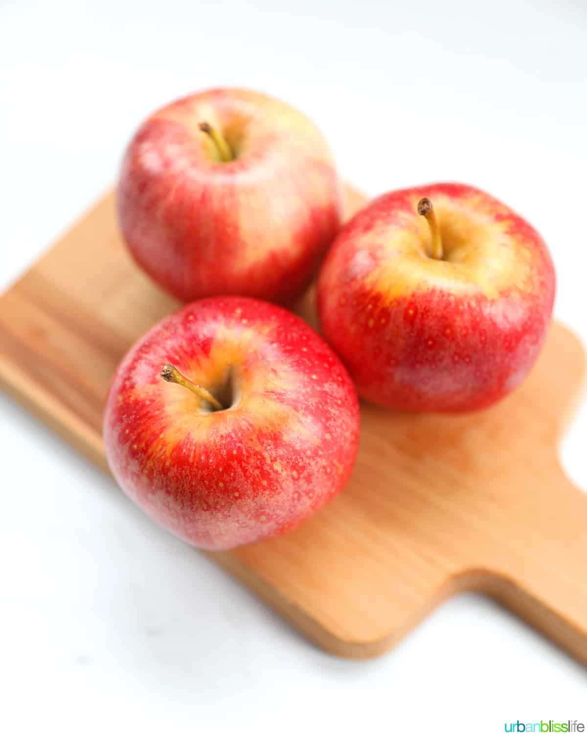 three gala apples on a wood cutting board.