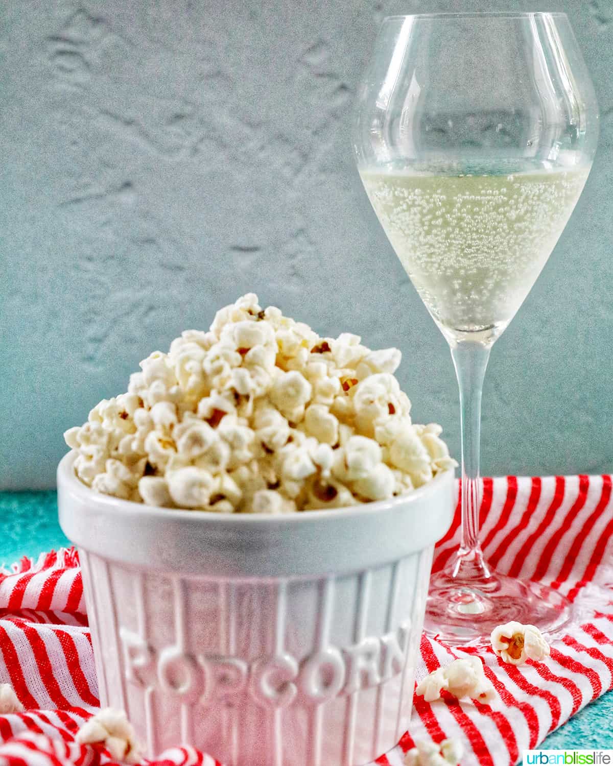 white popcorn bowl full of Instant Pot Popcorn on a red and white napkin with glass of sparkling wine behind it.