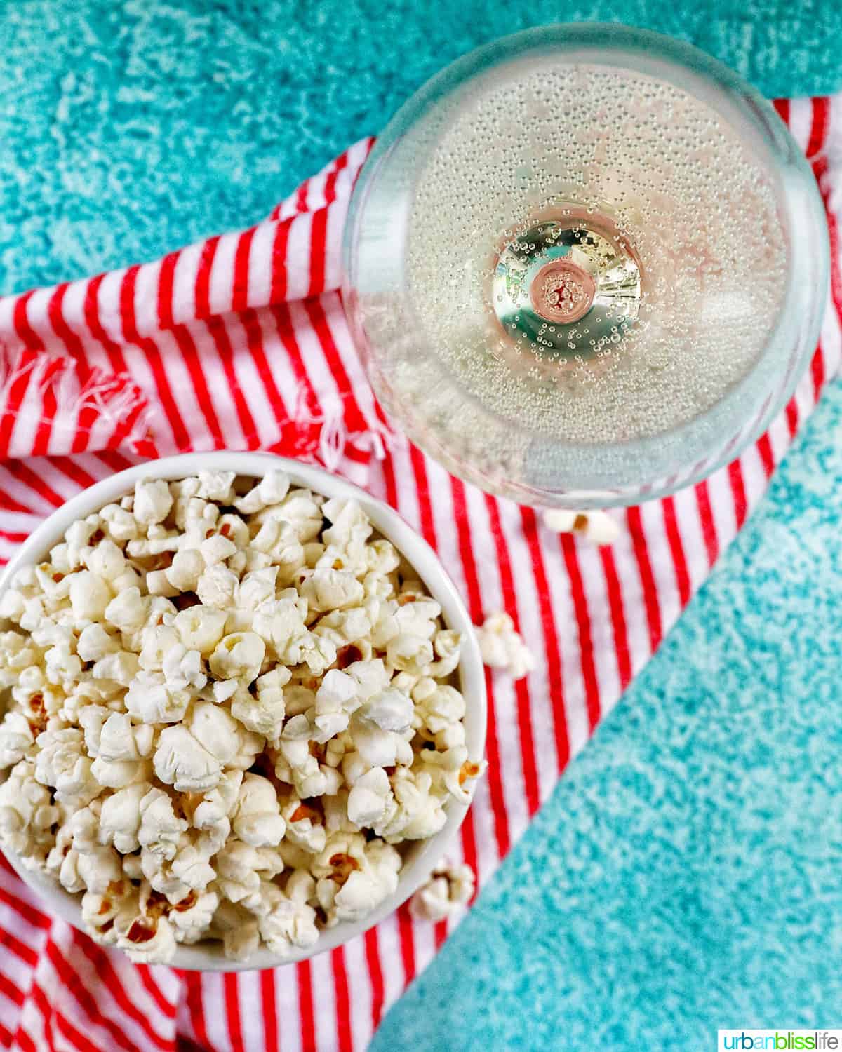 overhead photo of white popcorn bowl full of Instant Pot Popcorn on a red and white napkin with a glass of sparkling wine.