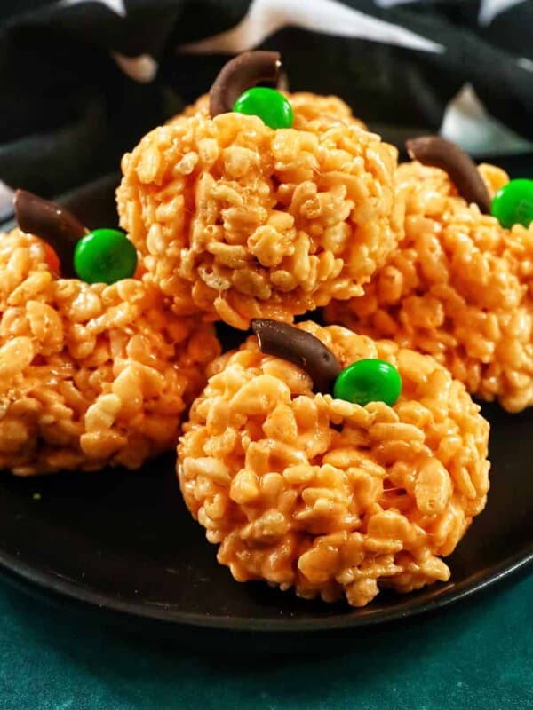four pumpkin rice krispie treats on a black plate.