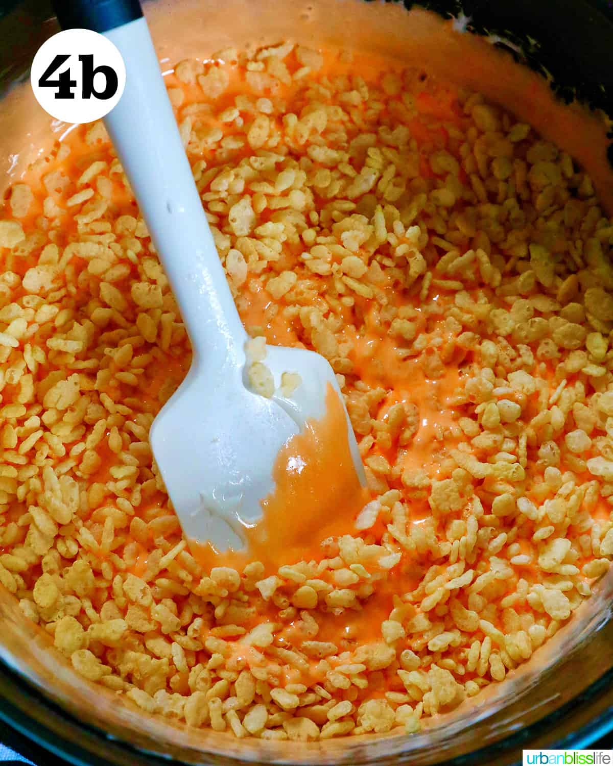 spatula stirring rice krispies cereal in orange marshmallow mixture.