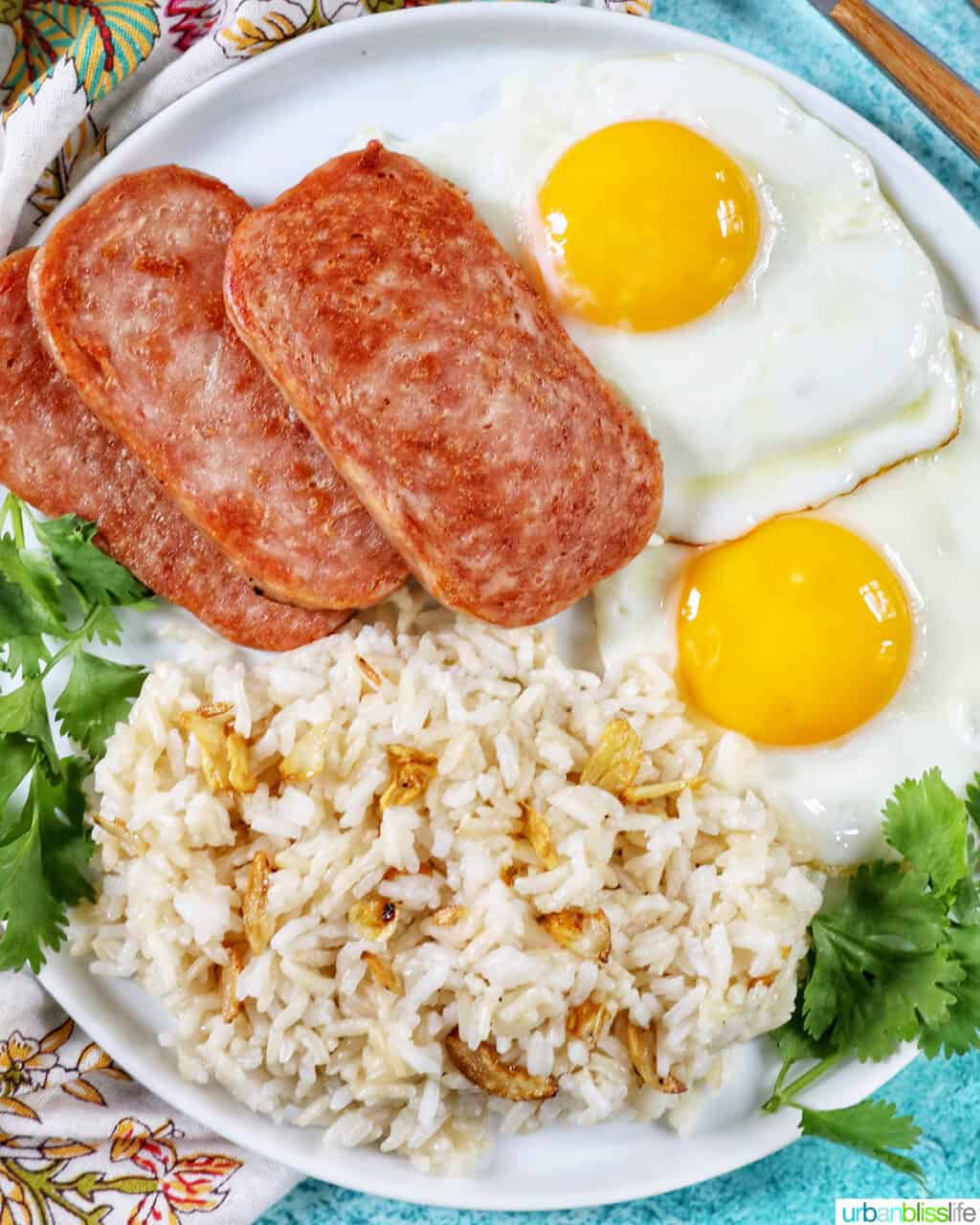 Plate of Spamsilog: slices of Spam, two eggs over easy, and Filipino Sinangag garlic rice with greens.