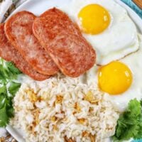 Plate of Spamsilog: slices of Spam, two eggs over easy, and Filipino Sinangag garlic rice with greens.