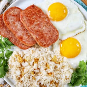 Plate of Spamsilog: slices of Spam, two eggs over easy, and Filipino Sinangag garlic rice with greens.