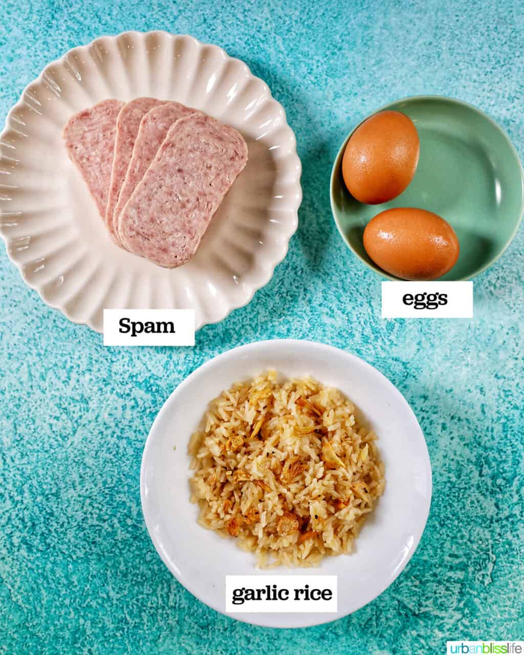 plates of spam, sinangag garlic rice, two eggs to make Filipino Spamsilog on a blue table.