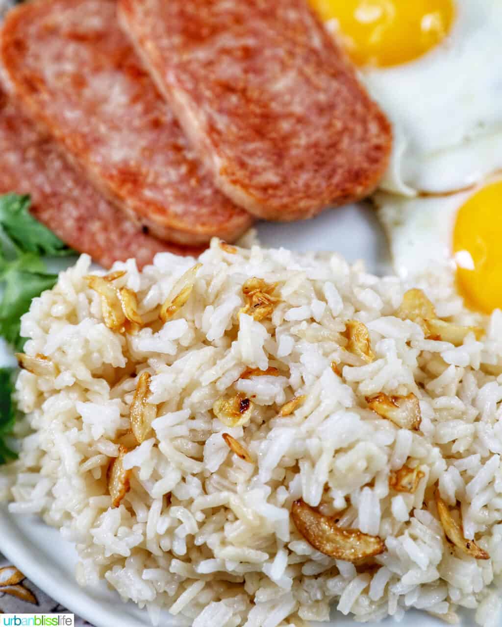 Plate of Spamsilog: slices of Spam, two eggs over easy, and Filipino Sinangag garlic rice with greens.