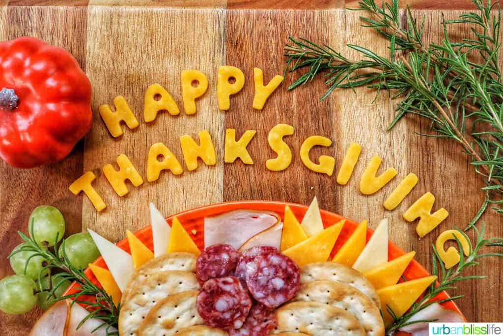 Cheese cut into letters stating Happy Thanksgiving at the top of a turkey charcuterie board.