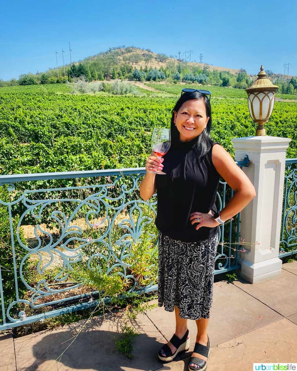 Marlynn Schotland holding a glass of rosé wine in front of Belle Fiore Winery vineyards