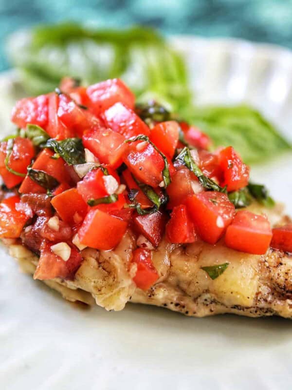 single bruschetta chicken on a white plate with basil leaves in the background.