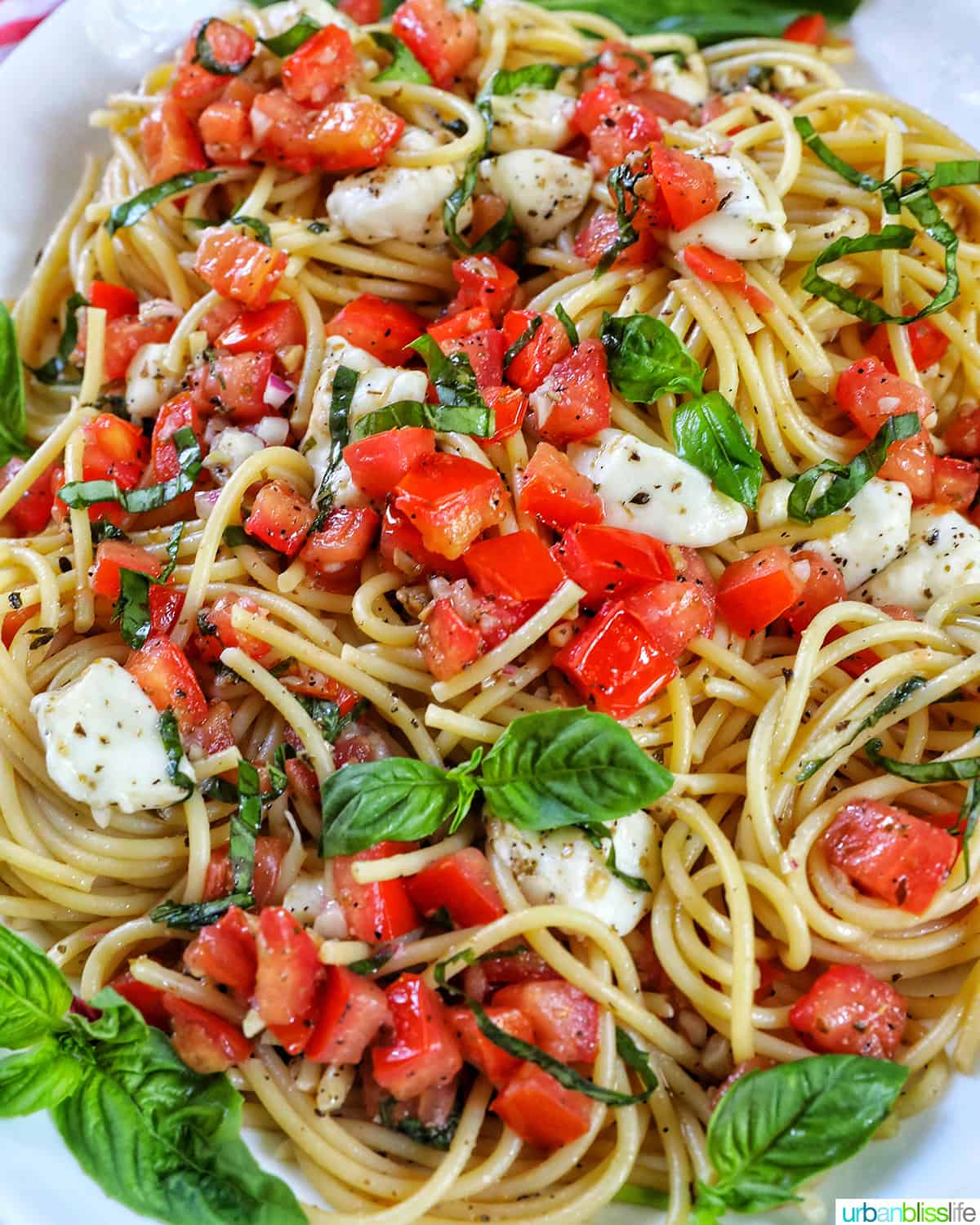 bruschetta pasta with tomatoes, basil, mozzarella cheese in a big white serving bowl.