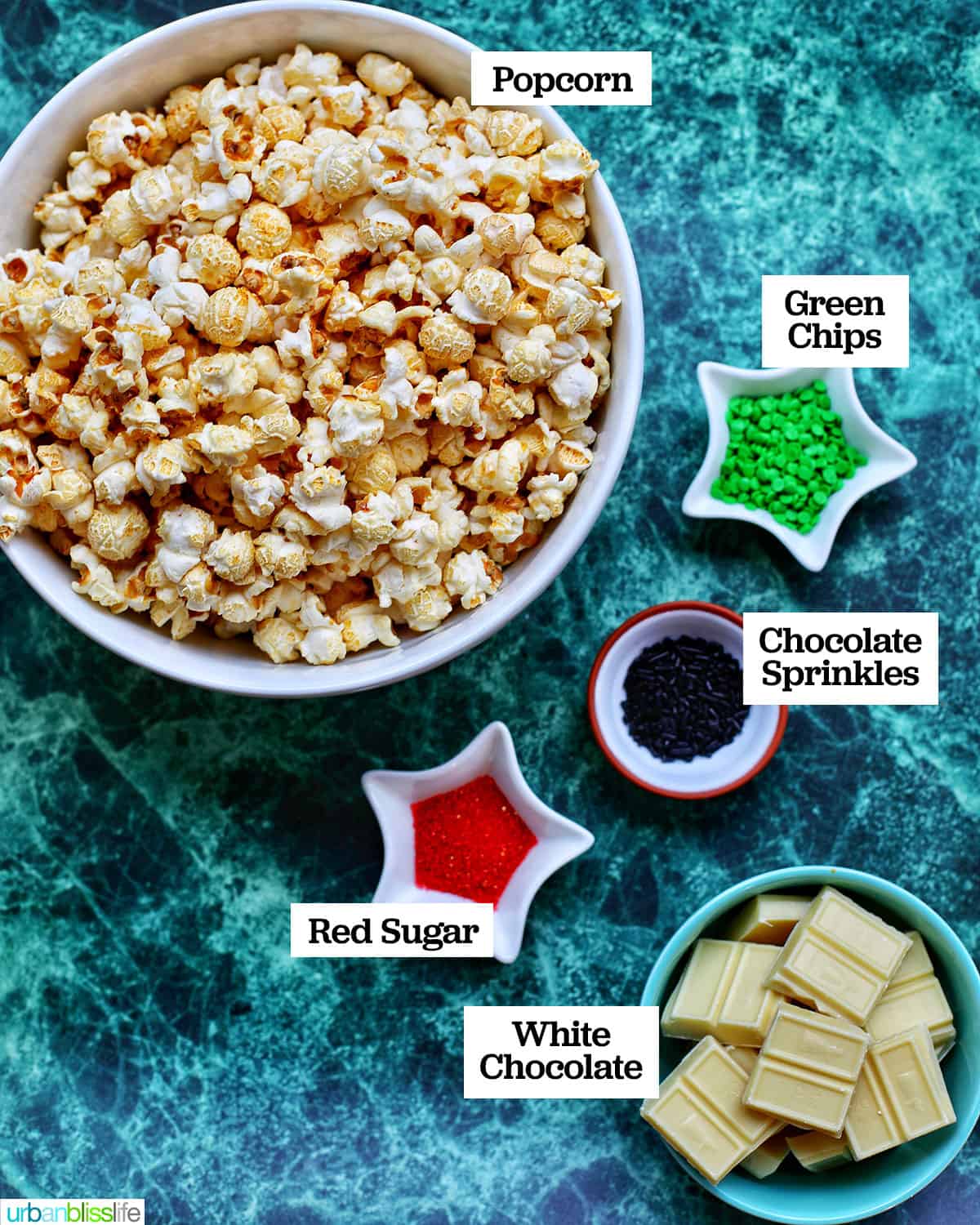 bowls of ingredients to make Christmas popcorn on a green table.
