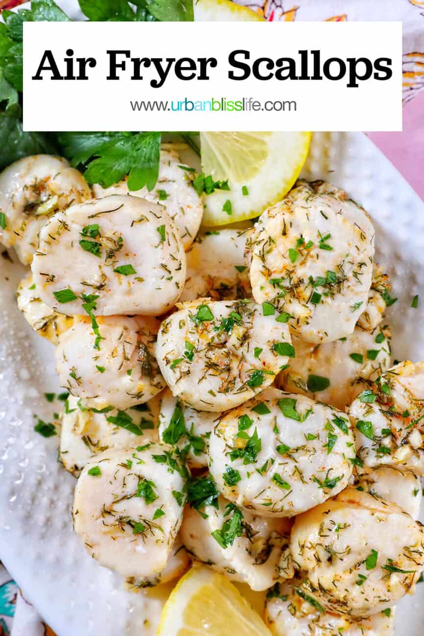 several cooked scallops topped with herbs and garlic, with lemon slices and parsley, on a white plate with text overlay.