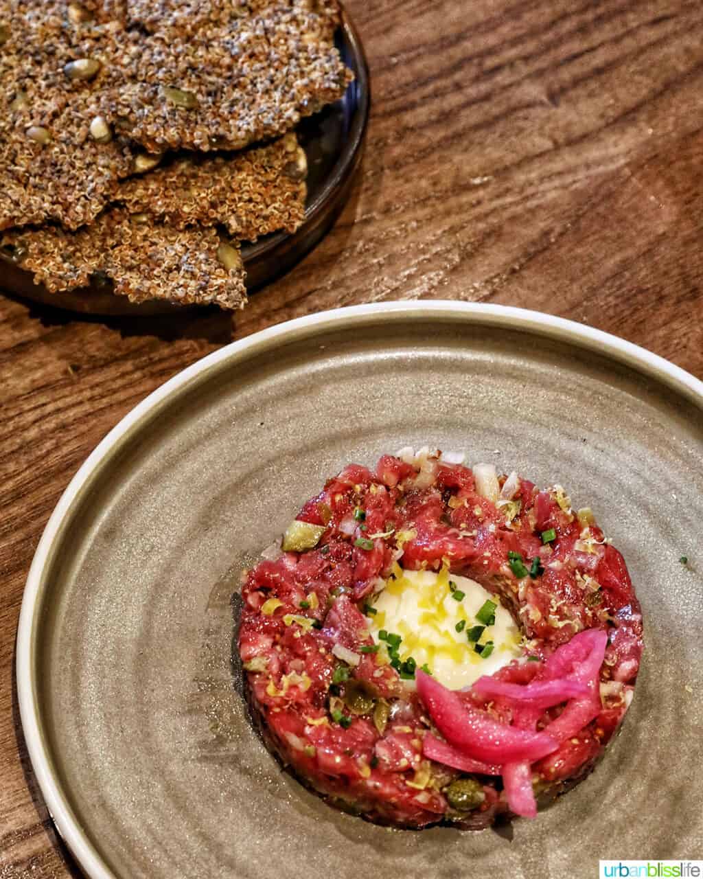 bison tartare on a cream colored plate with side of crackers.