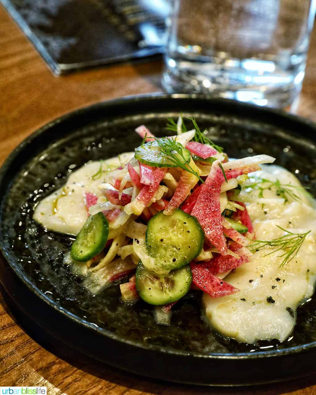 Tuna crudo with veggies on a dark plate.