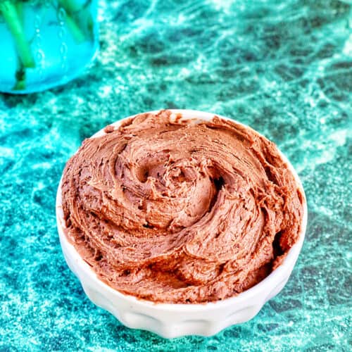 chocolate buttercream frosting in a white bowl on a green marble table.