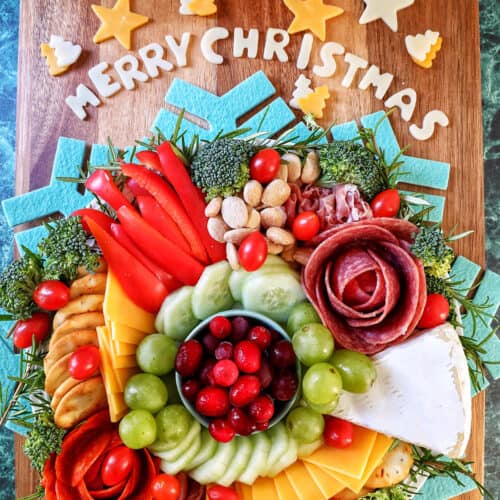 Christmas charcuterie board with meats, cheeses, fruits, veggies, crackers, and Merry Christmas in cheese letters on a cutting board.