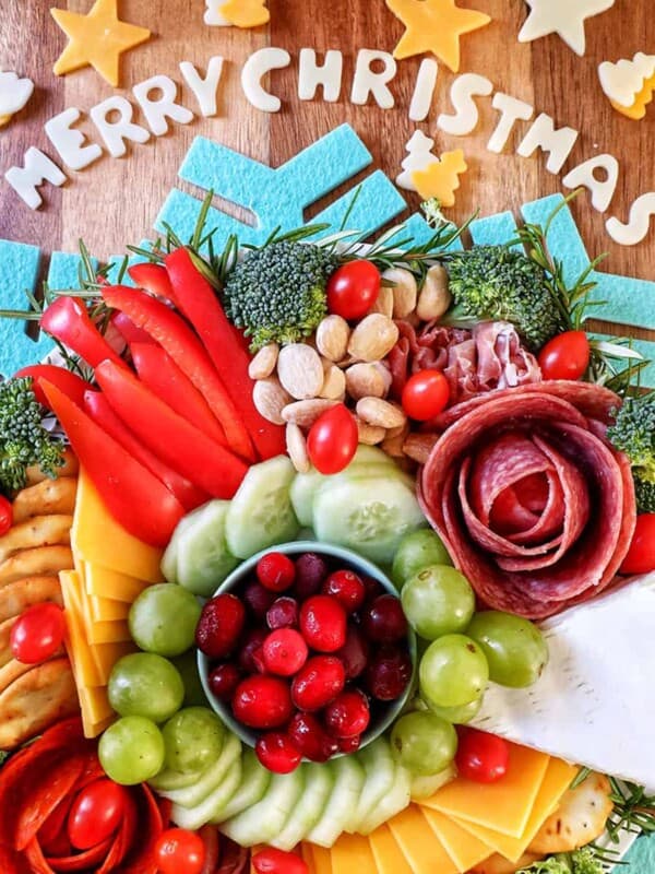 Christmas charcuterie board with meats, cheeses, fruits, veggies, crackers, and Merry Christmas in cheese letters on a cutting board.