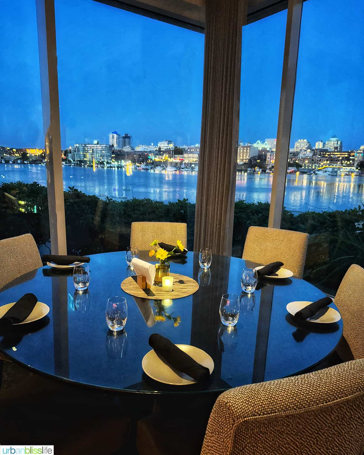 round dinner table and chairs with a view of Victoria Harbour at Aura restaurant inside the Inn at Laurel Point hotel.