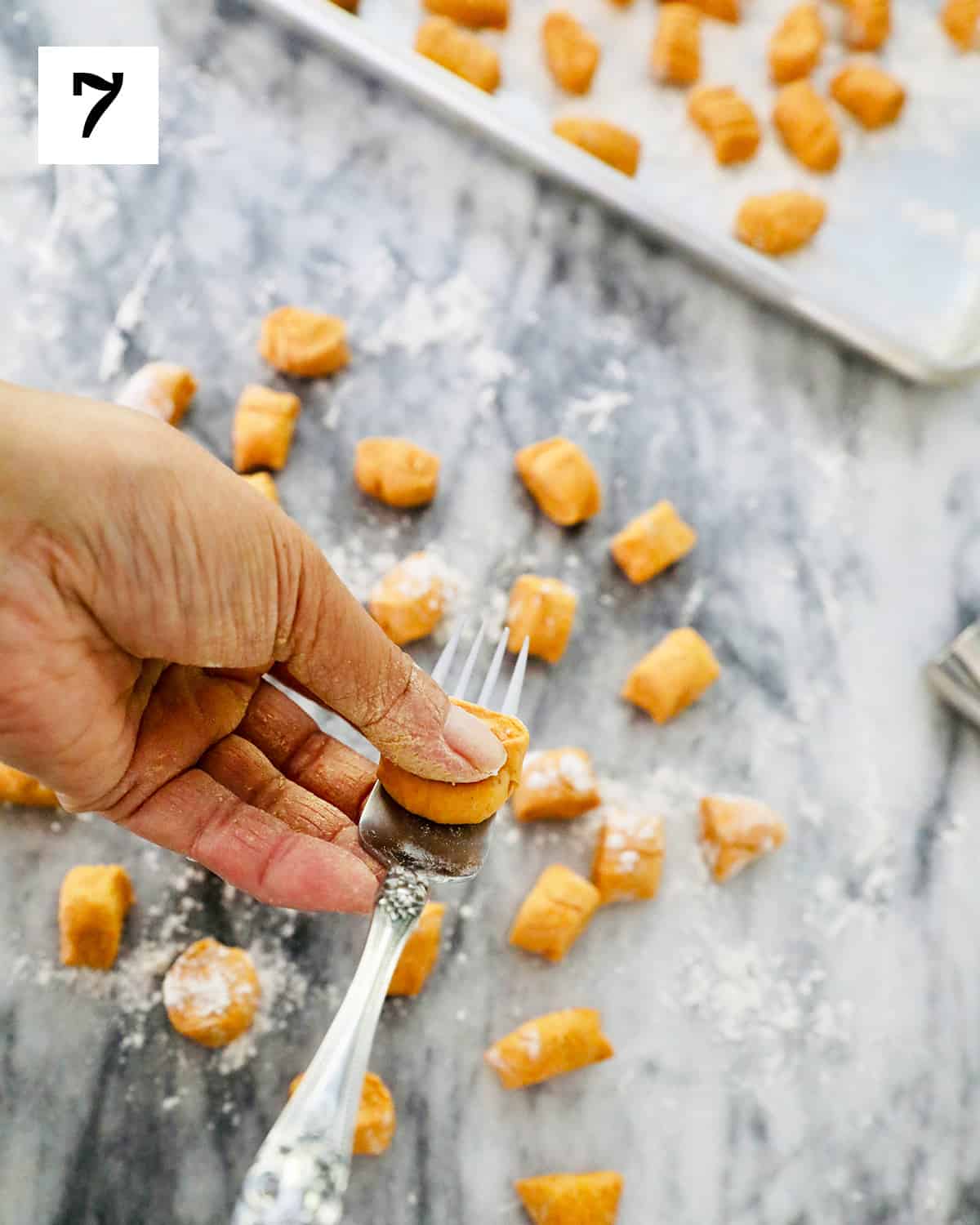 shaping pumpkin gnocchi with a fork over marble countertop.