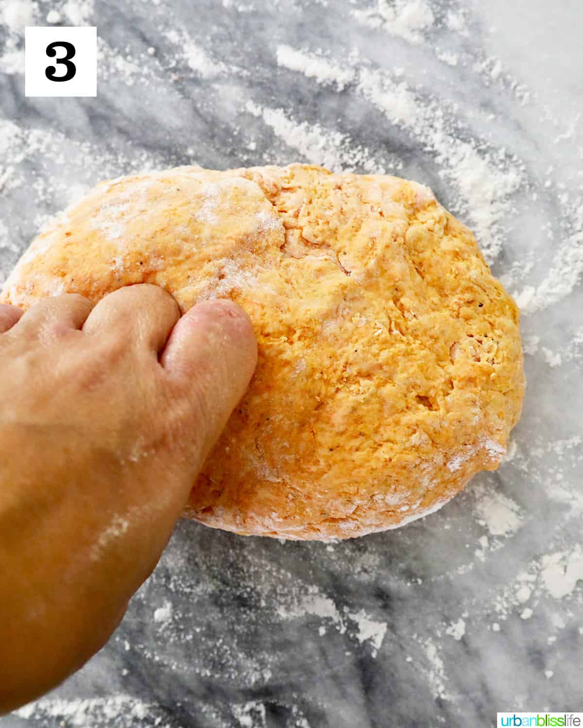 kneading pumpkin gnocchi dough on a marble countertop.