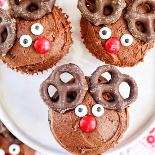 three reindeer cupcakes with chocolate buttercream frosting on a plate.